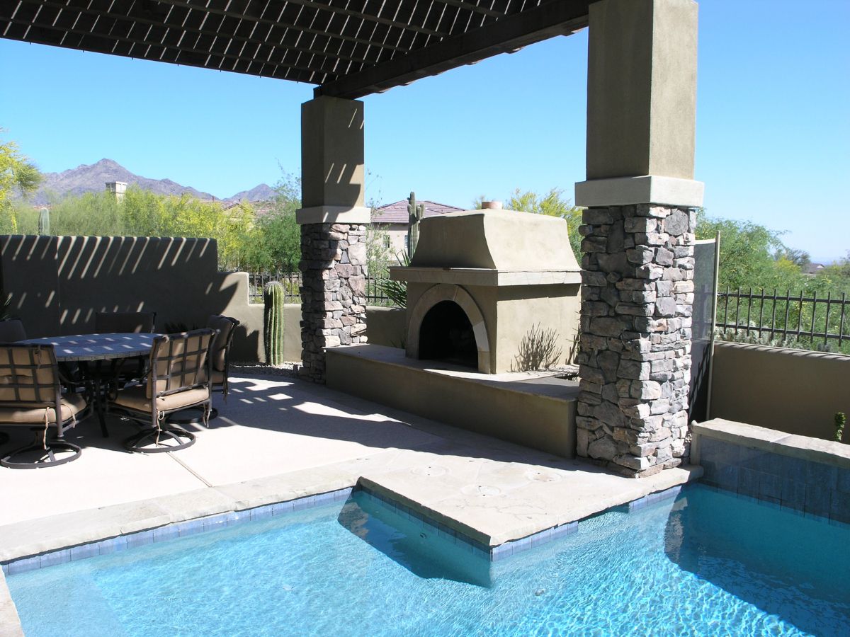 Outdoor pool patio with stone fireplace, shaded pergola, dining set and desert mountain views