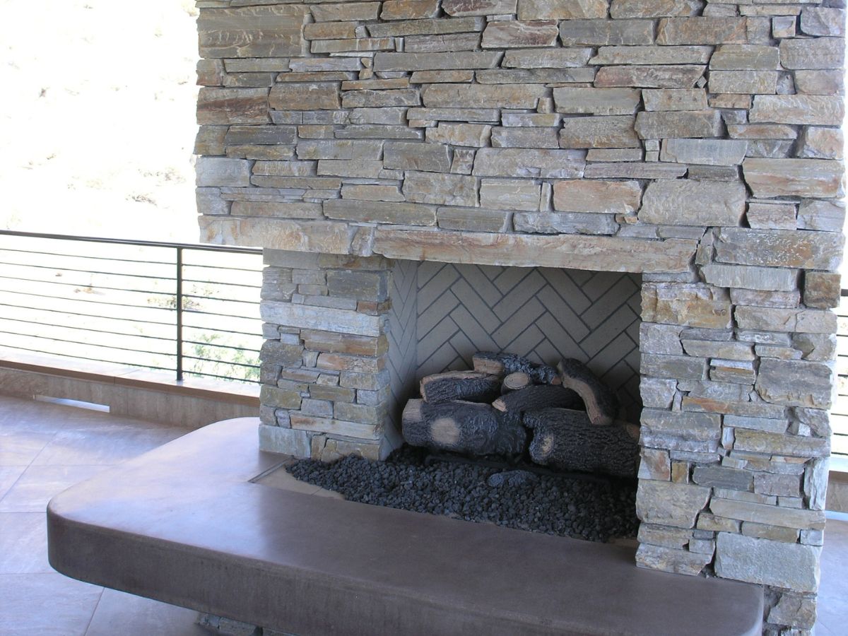 Stacked-stone outdoor fireplace with gas logs on concrete hearth bench, patio railing and tiled floor