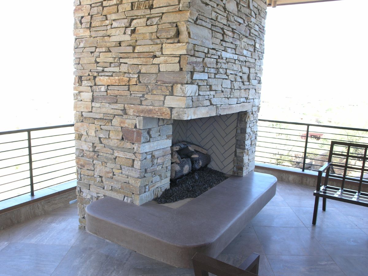 Modern outdoor stacked-stone fireplace with built-in concrete bench on covered patio overlooking desert landscape