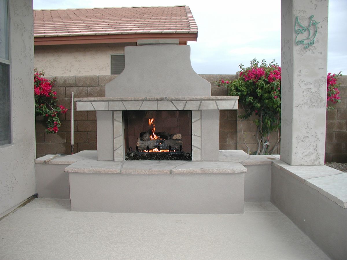 Built-in stucco outdoor fireplace with stone mantel and gas logs on backyard patio flanked by pink bougainvillea