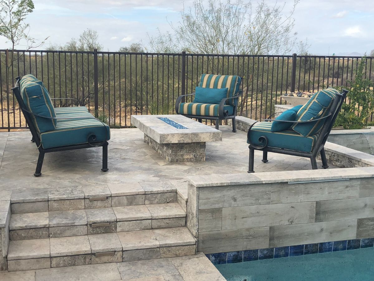 Poolside patio furniture: teal-striped cushioned chairs around a stone fire table with a desert view