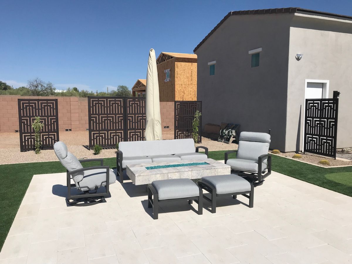 Backyard patio with modern gray cushioned outdoor seating, fire glass table, white pavers and decorative privacy screens