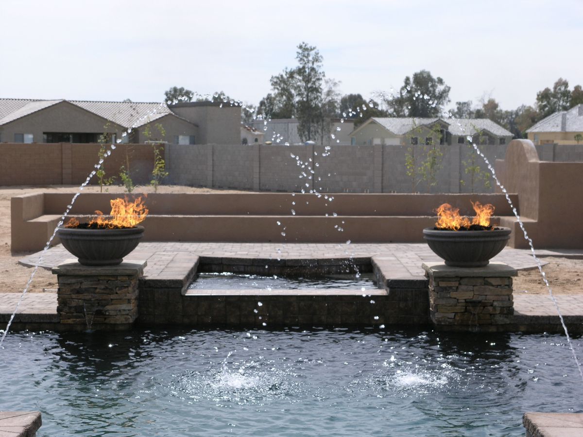 Backyard pool with arcing fountain jets and twin fire bowls on stone pedestals, modern patio water feature