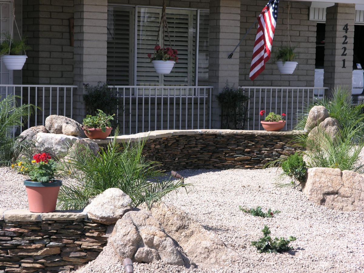 Xeriscape front yard with gravel, stacked stone retaining walls, potted plants and an American flag