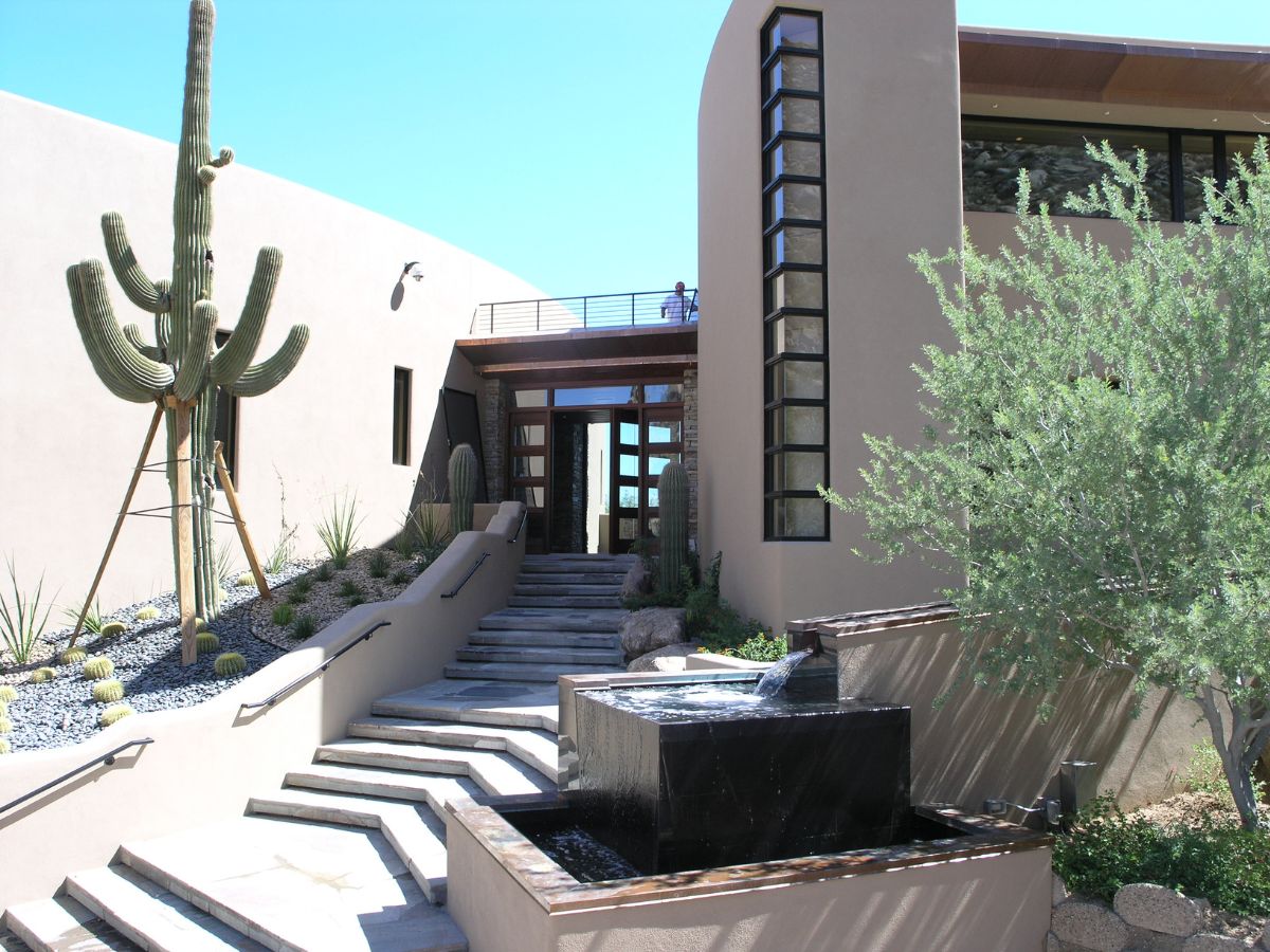 Modern desert home entrance with stone steps, black water fountain, large saguaro cactus and drought-tolerant landscaping.