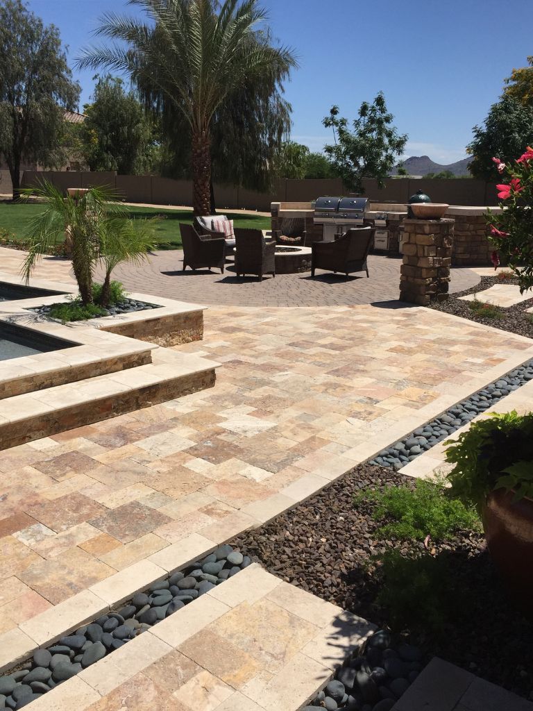 Sunlit backyard patio with travertine pavers, spa steps, lounge seating around a fire pit, built-in grill and palm trees
