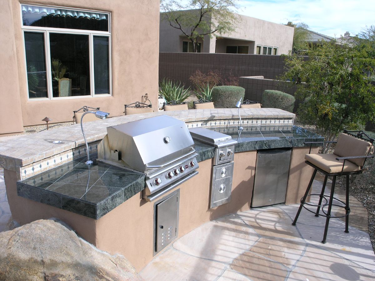 Outdoor backyard kitchen with stainless steel built-in grill, granite countertops, mini fridge and bar stool