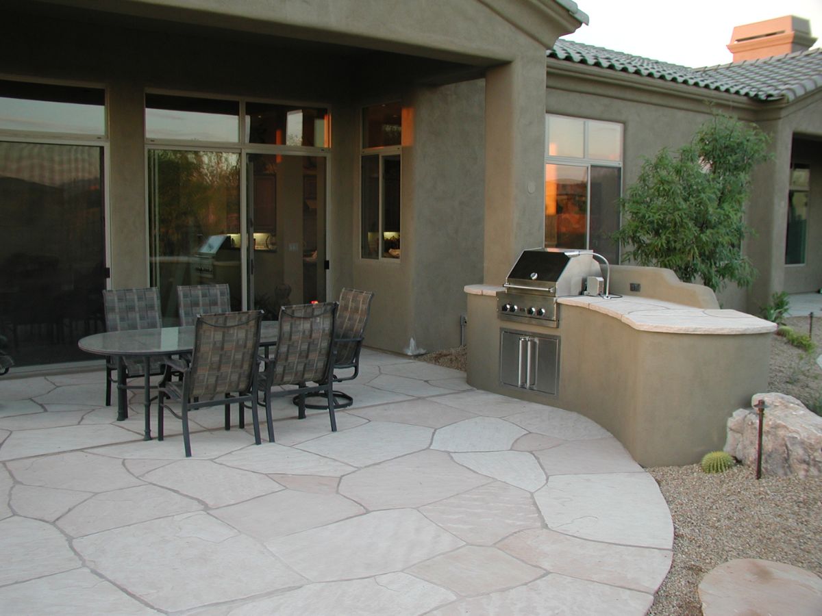 Stone backyard patio with outdoor dining set and built-in stainless steel grill, modern stucco home outdoor kitchen