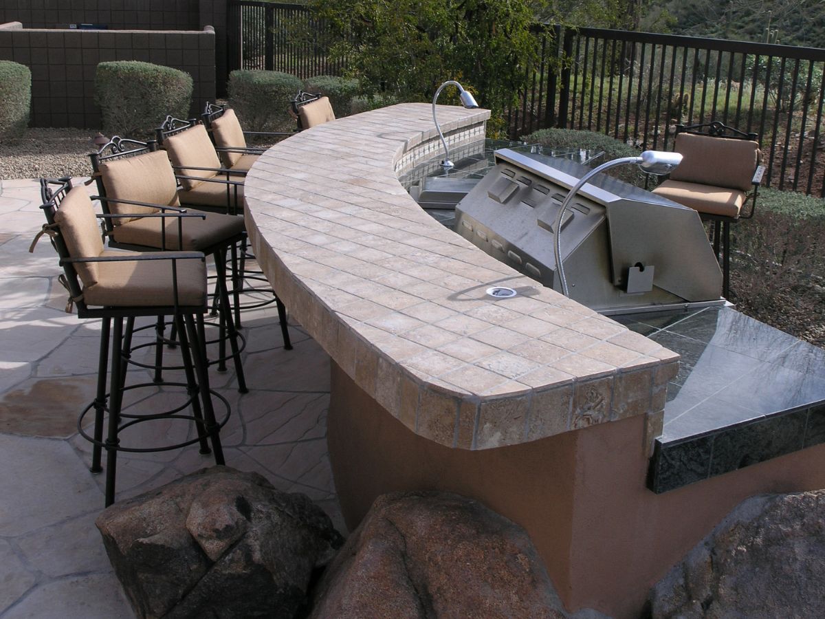 Outdoor kitchen with curved tiled bar countertop, cushioned swivel bar stools and built-in stainless steel grill