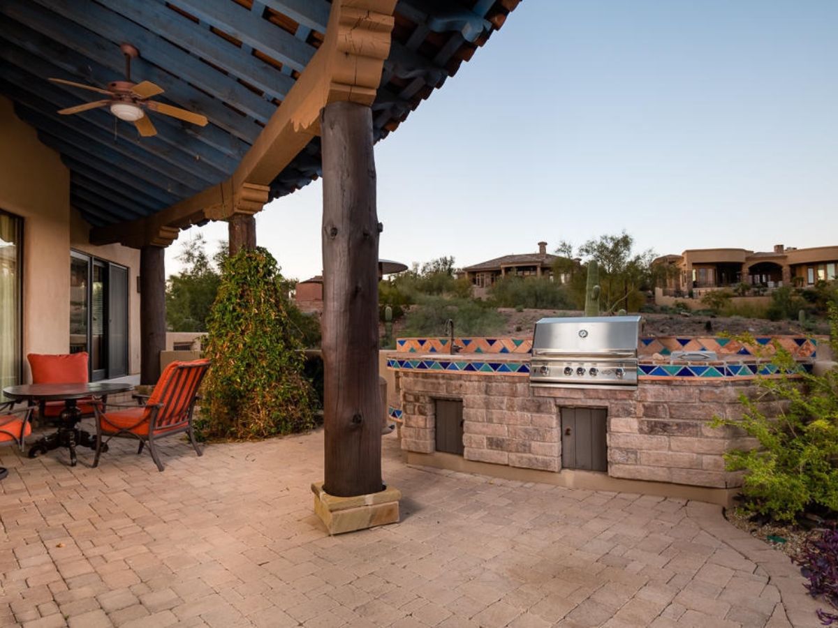 Southwestern patio with wooden pergola, tiled built-in stainless steel grill, outdoor seating and desert landscaping