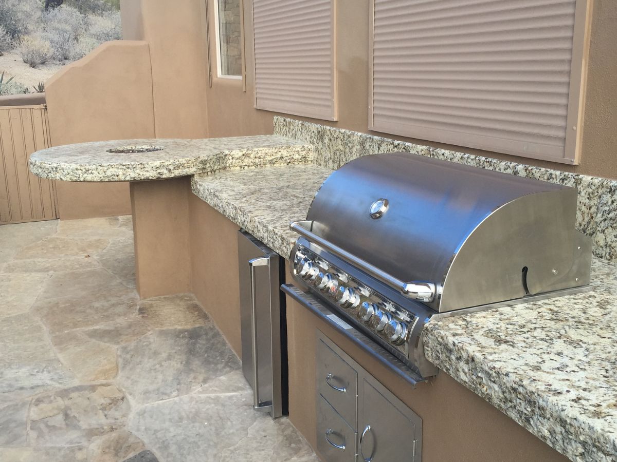 Built-in stainless steel gas grill in outdoor kitchen with granite countertops on stone patio