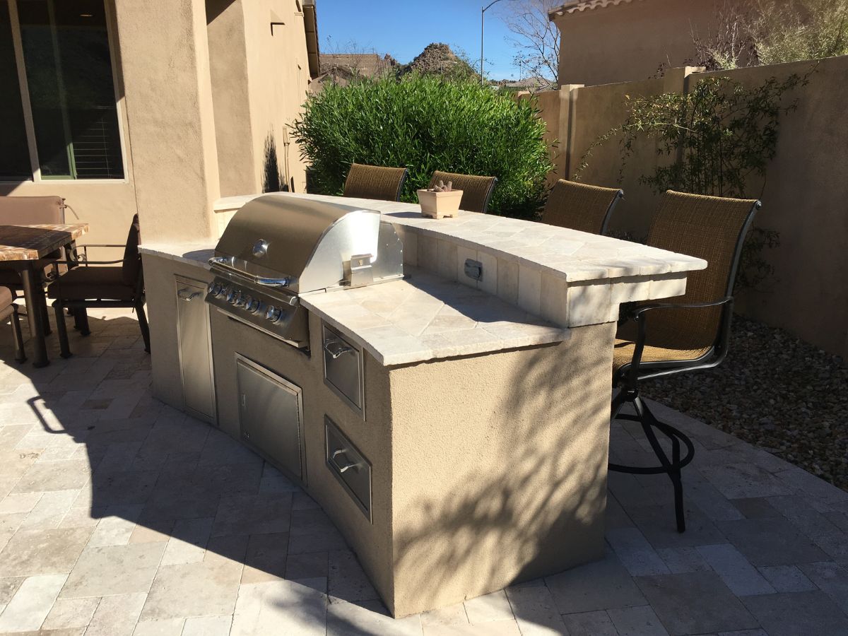 Outdoor kitchen with stainless steel built-in grill, stone countertop island and bar seating on tiled patio
