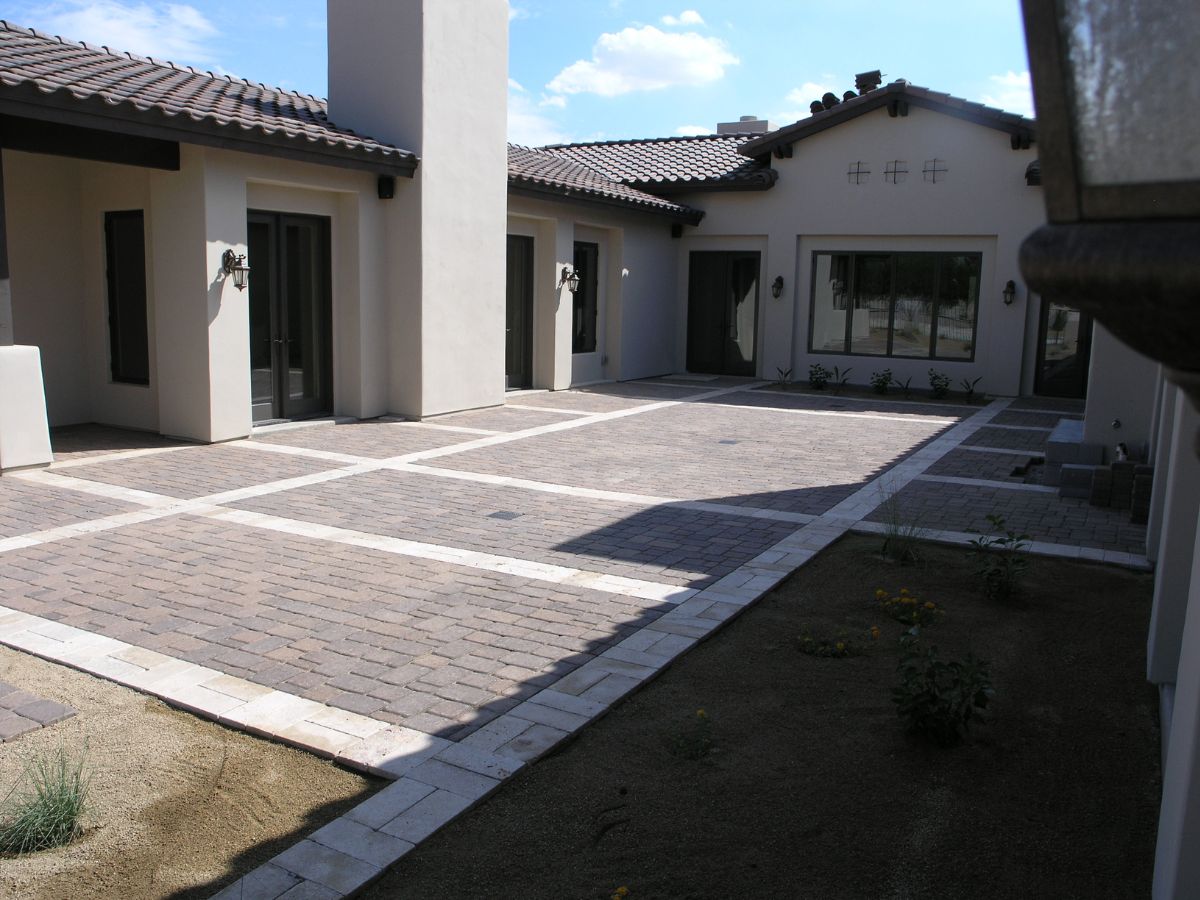 Spanish-style courtyard with grid-pattern paver patio, light stone borders, stucco walls and glass doors