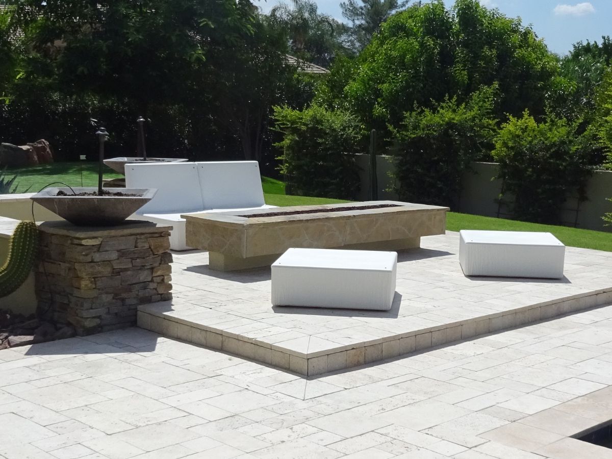 Modern backyard patio with travertine pavers, stone fire pit planter and white outdoor lounge seating.