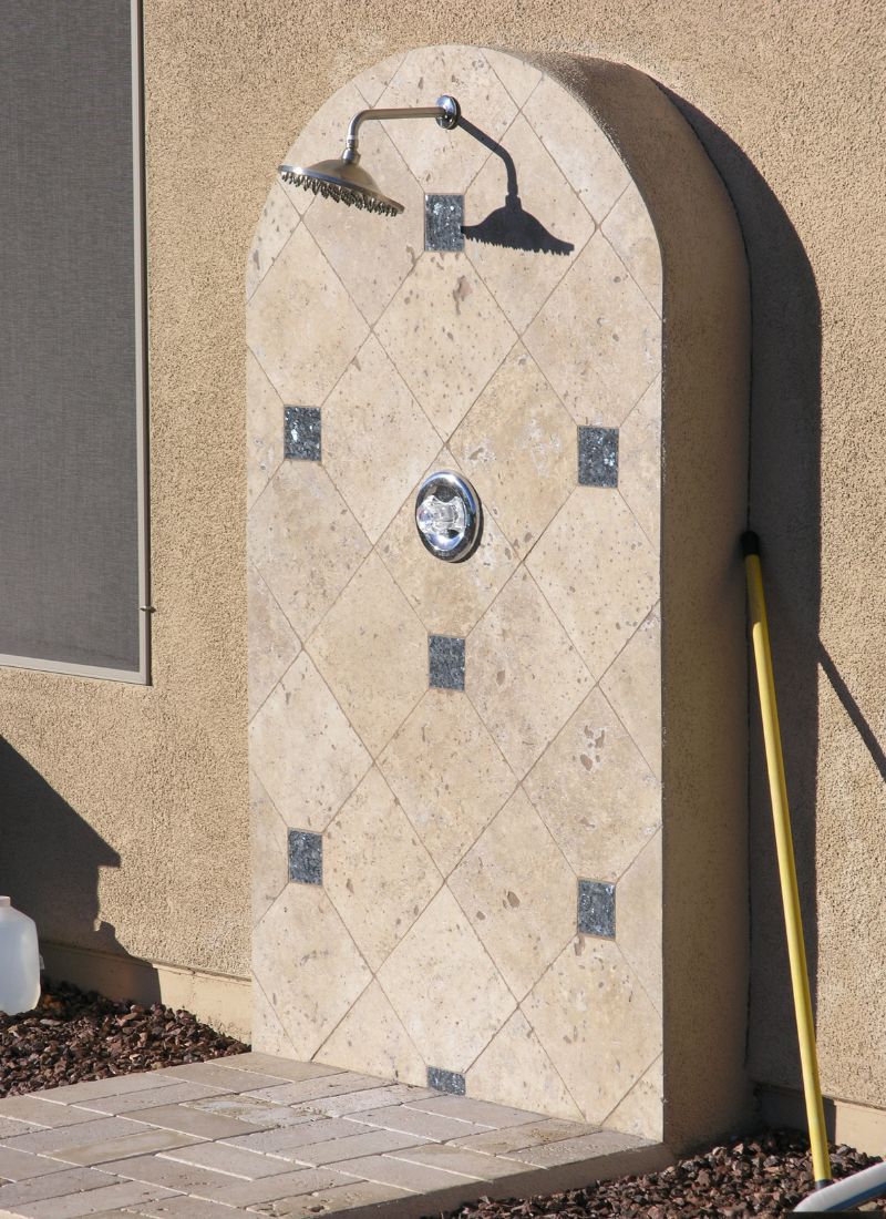 Backyard outdoor arched stone tile shower with rain showerhead and chrome control on stucco wall