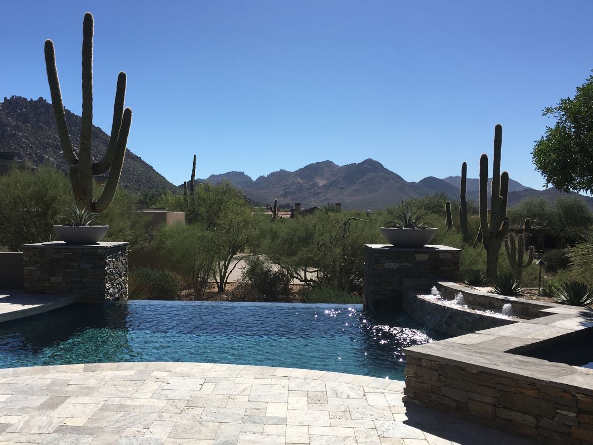 Infinity pool with mountain view and saguaro cacti in desert backyard under clear blue sky