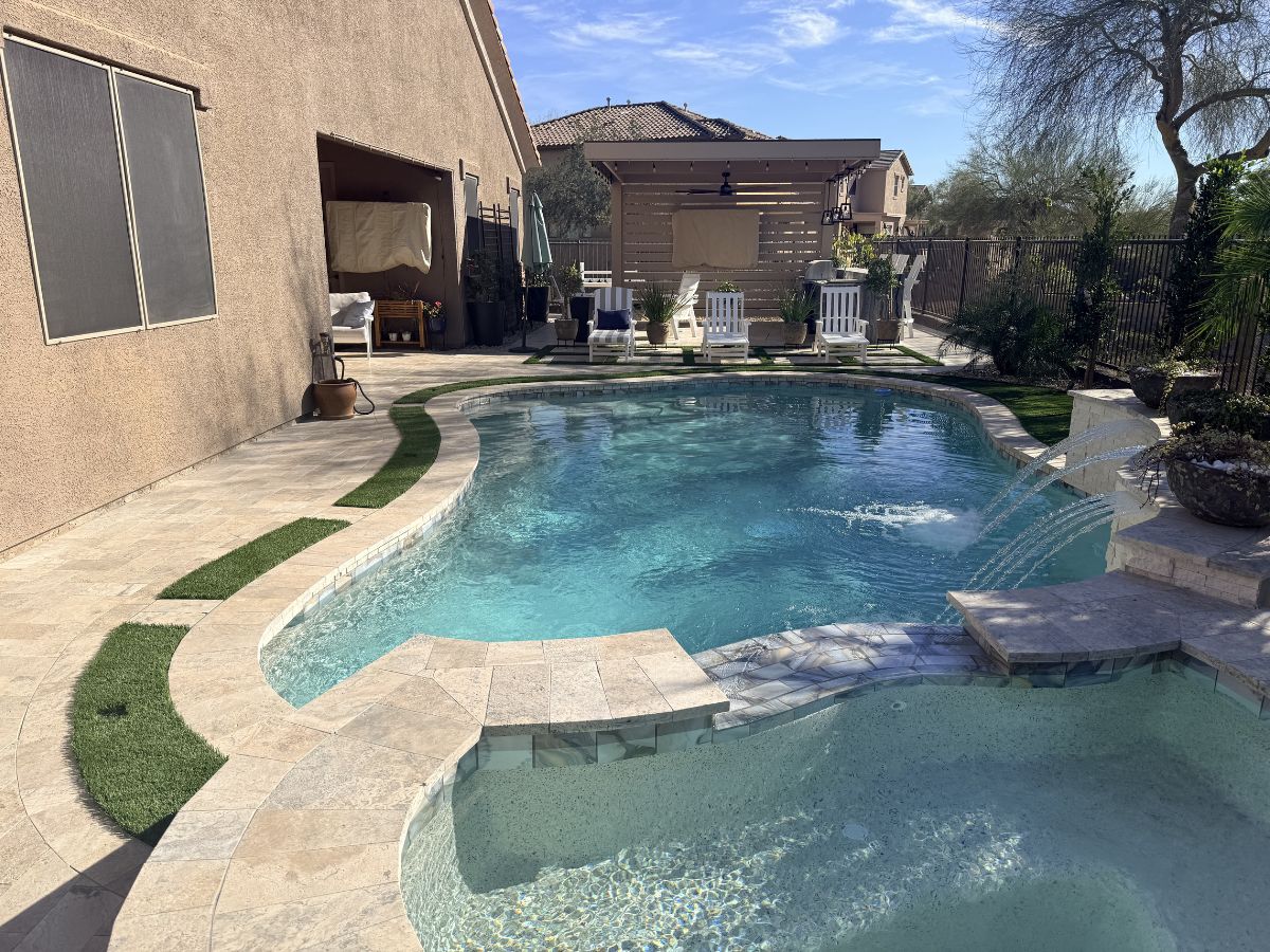 Luxury backyard pool and spa with travertine deck, water fountains, pergola seating area and lounge chairs in sunny yard