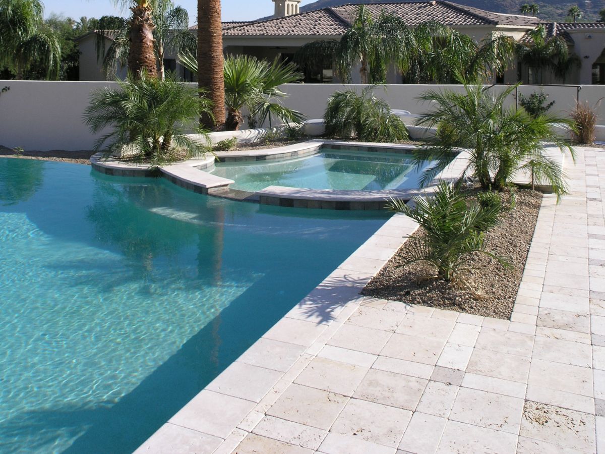 Resort-style backyard pool and elevated spa with palm trees, travertine tile deck and desert landscaping in modern home.