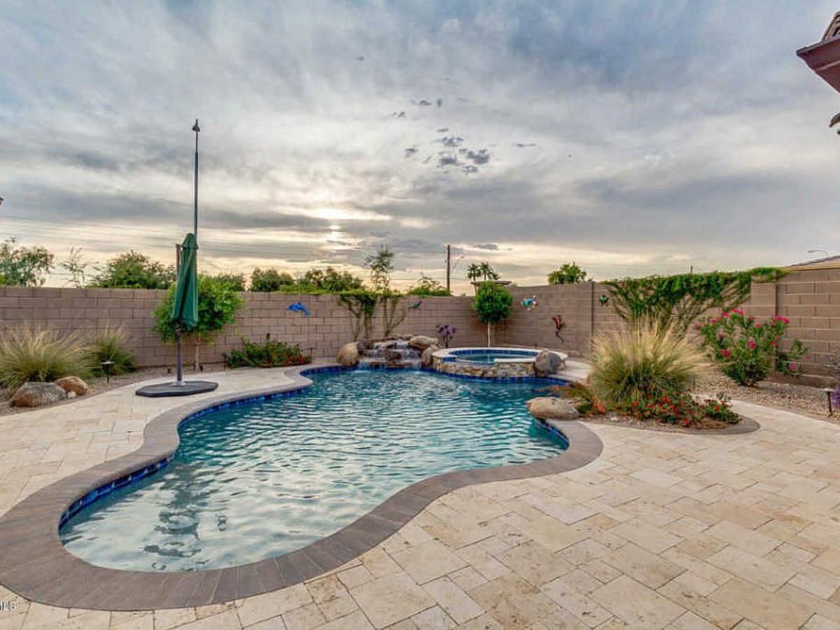 Backyard swimming pool with attached spa, stone paver patio, landscaped beds and umbrella at sunset