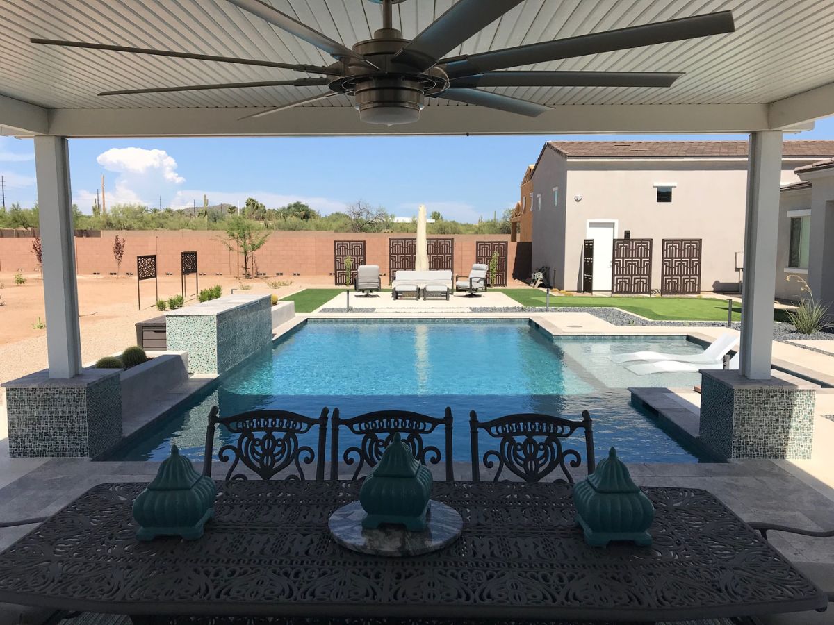Luxury backyard patio with covered dining area, ceiling fan, swimming pool, lounge chairs and desert landscaping