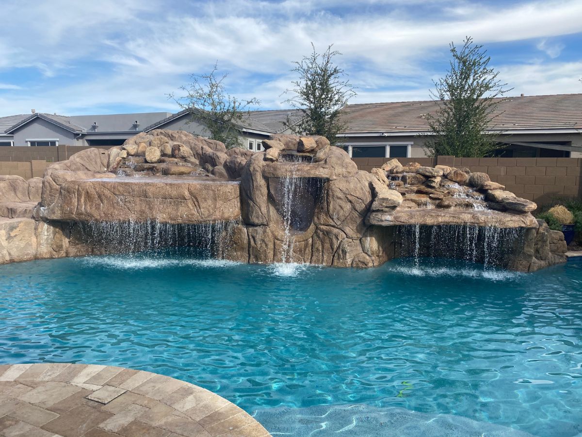 Backyard swimming pool with artificial rock waterfalls and grotto, cascading water and clear turquoise pool