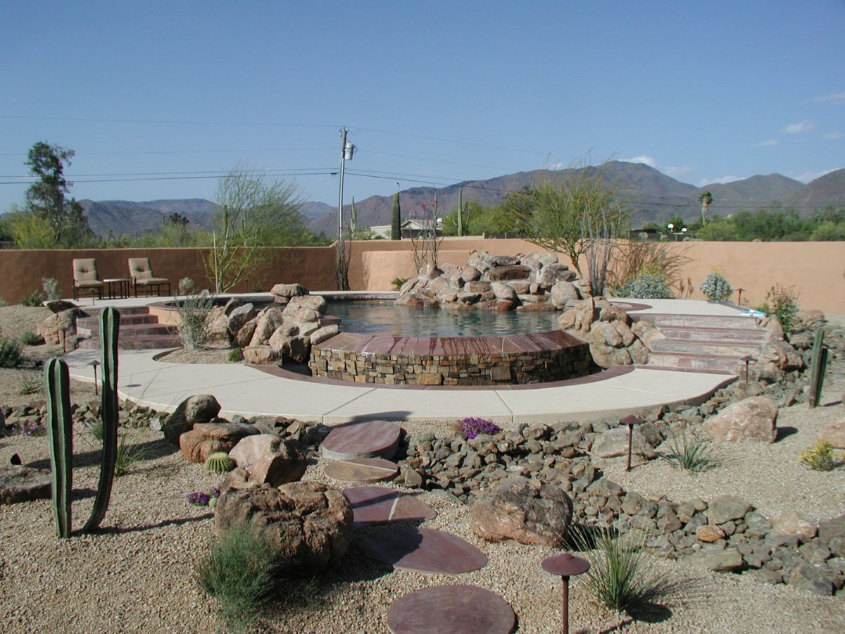 Desert backyard pool and circular rock spa with waterfall, stone patio, cacti xeriscape and mountain views