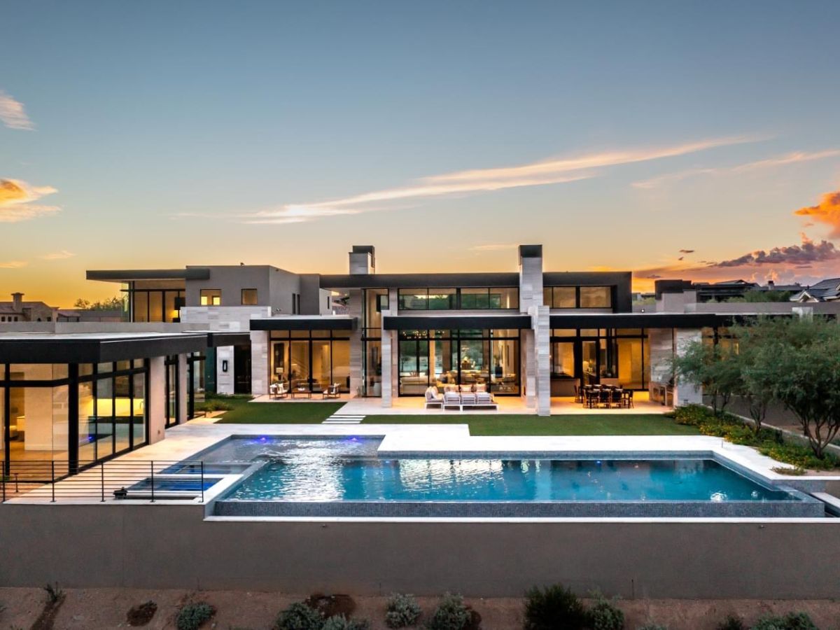 Modern luxury desert mansion with floor-to-ceiling windows and an illuminated infinity pool at sunset