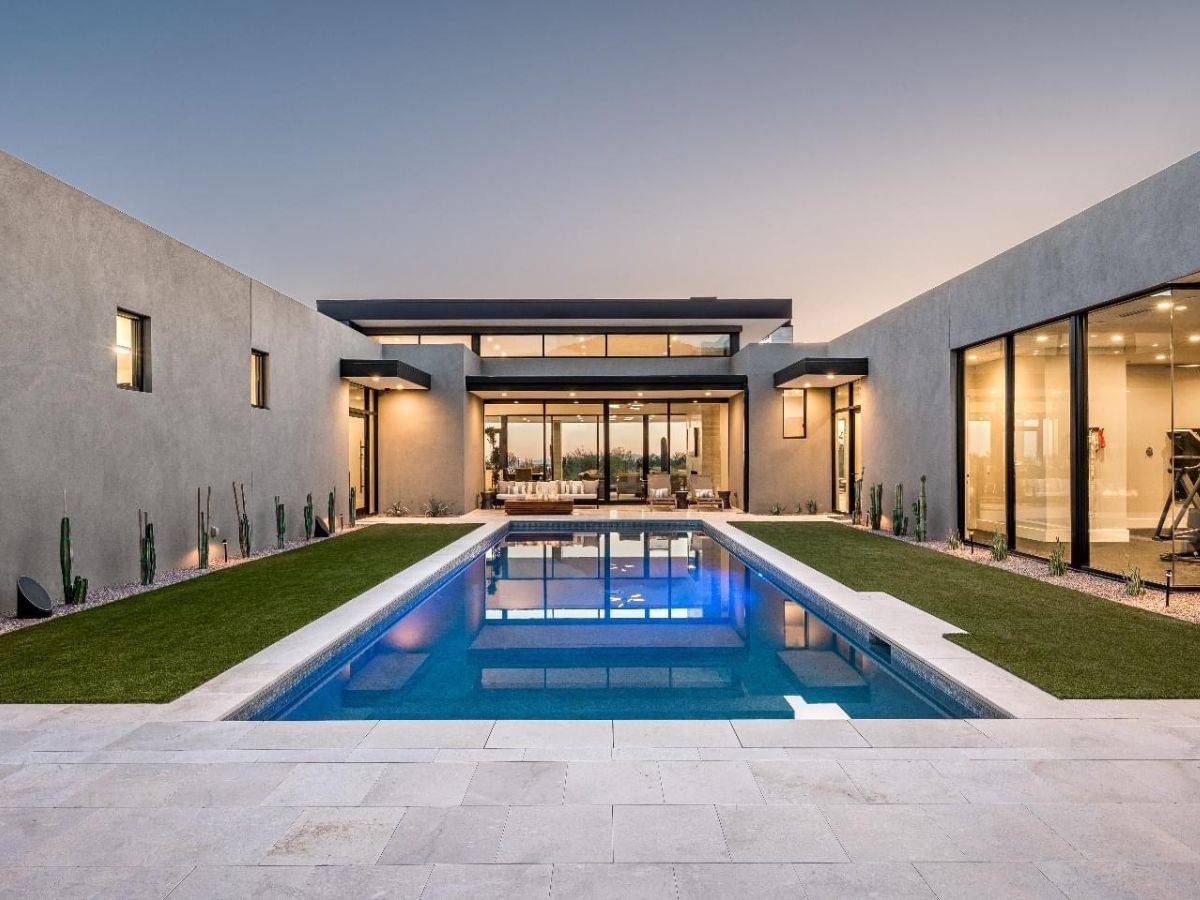 Modern luxury home courtyard with rectangular pool and floor-to-ceiling glass walls at dusk