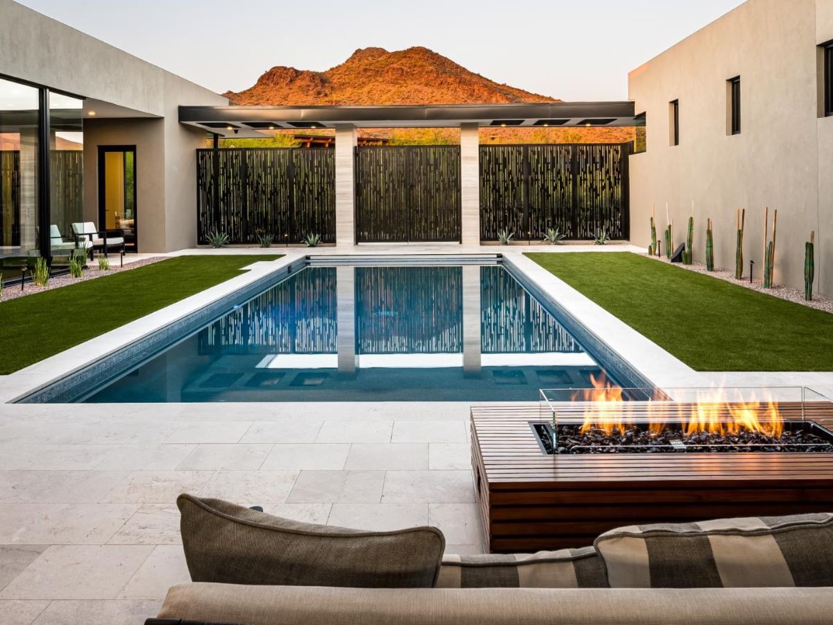 Modern luxury backyard with rectangular swimming pool, built-in fire pit, patio seating and mountain backdrop