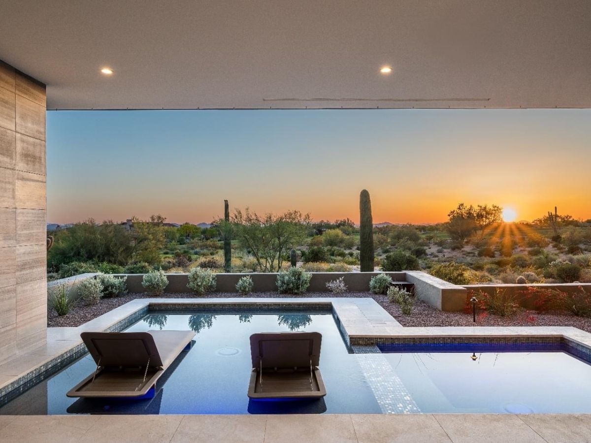 Luxury modern patio with two in-pool lounge chairs overlooking a desert landscape with saguaro cacti at sunset