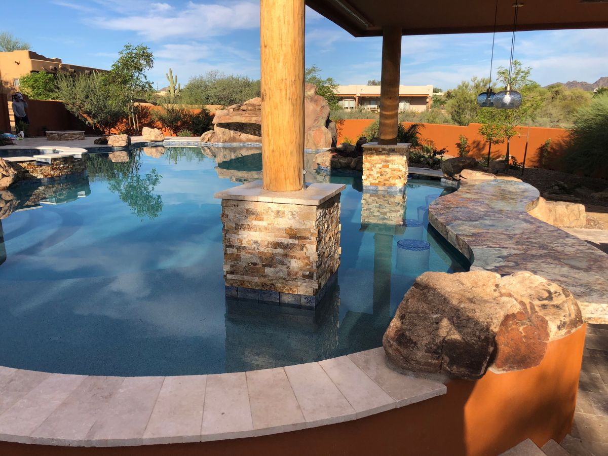 Luxury backyard resort-style pool with swim-up bar, stone pillars and natural rock features amid desert landscaping