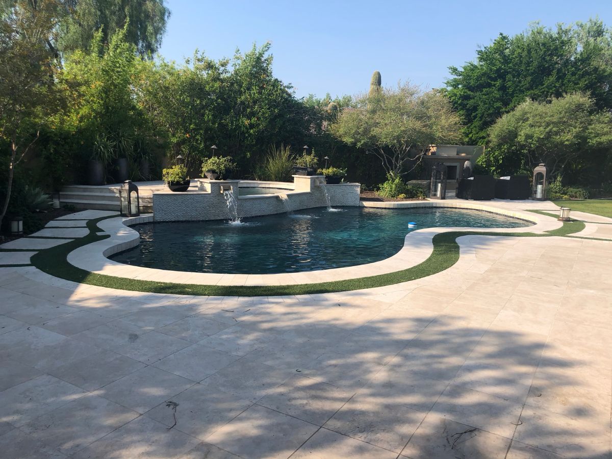 Luxury backyard pool with waterfalls and spa, travertine patio, curved design and lush landscaping
