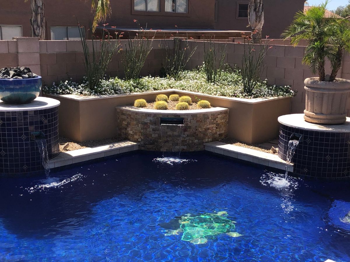 Backyard blue swimming pool with turtle mosaic, corner waterfalls, tiled columns and desert planters.