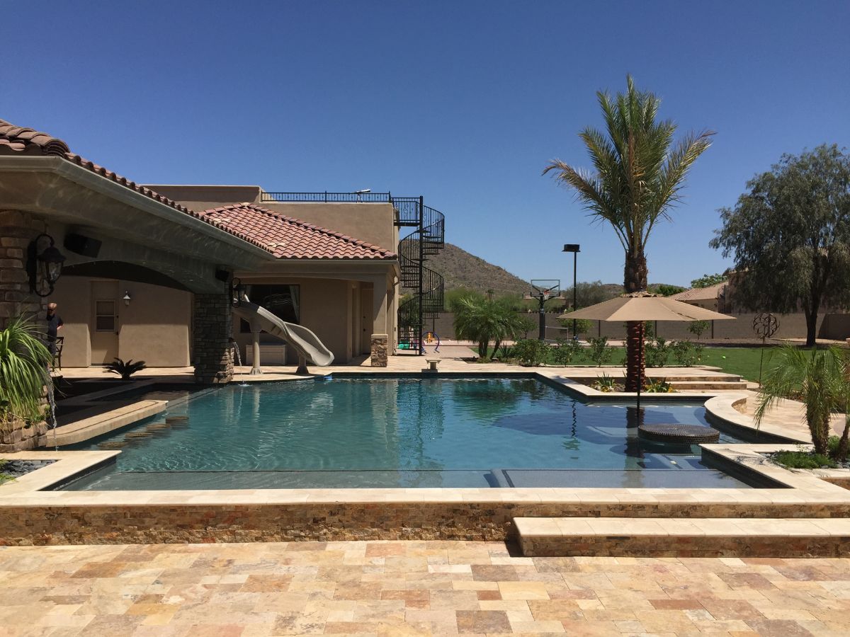 Luxury backyard pool with travertine patio, waterslide, swim-up umbrella table, palm tree and spiral staircase