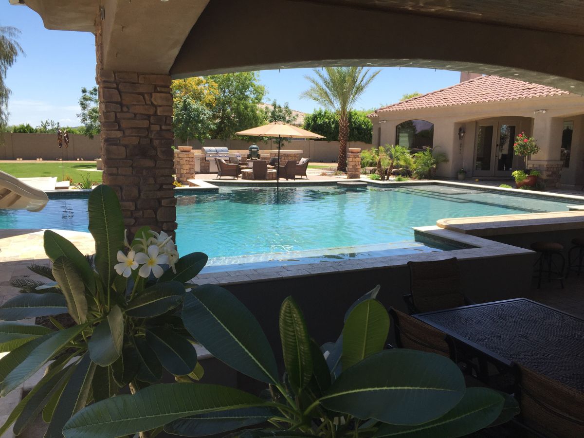 Luxury backyard swimming pool with covered patio, outdoor dining, umbrella seating, palm trees and spa