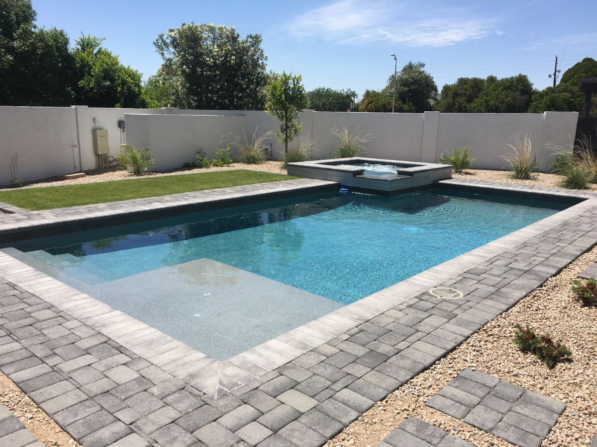 Modern backyard rectangular pool with raised spa, gray paver deck, gravel landscaping and clear blue water