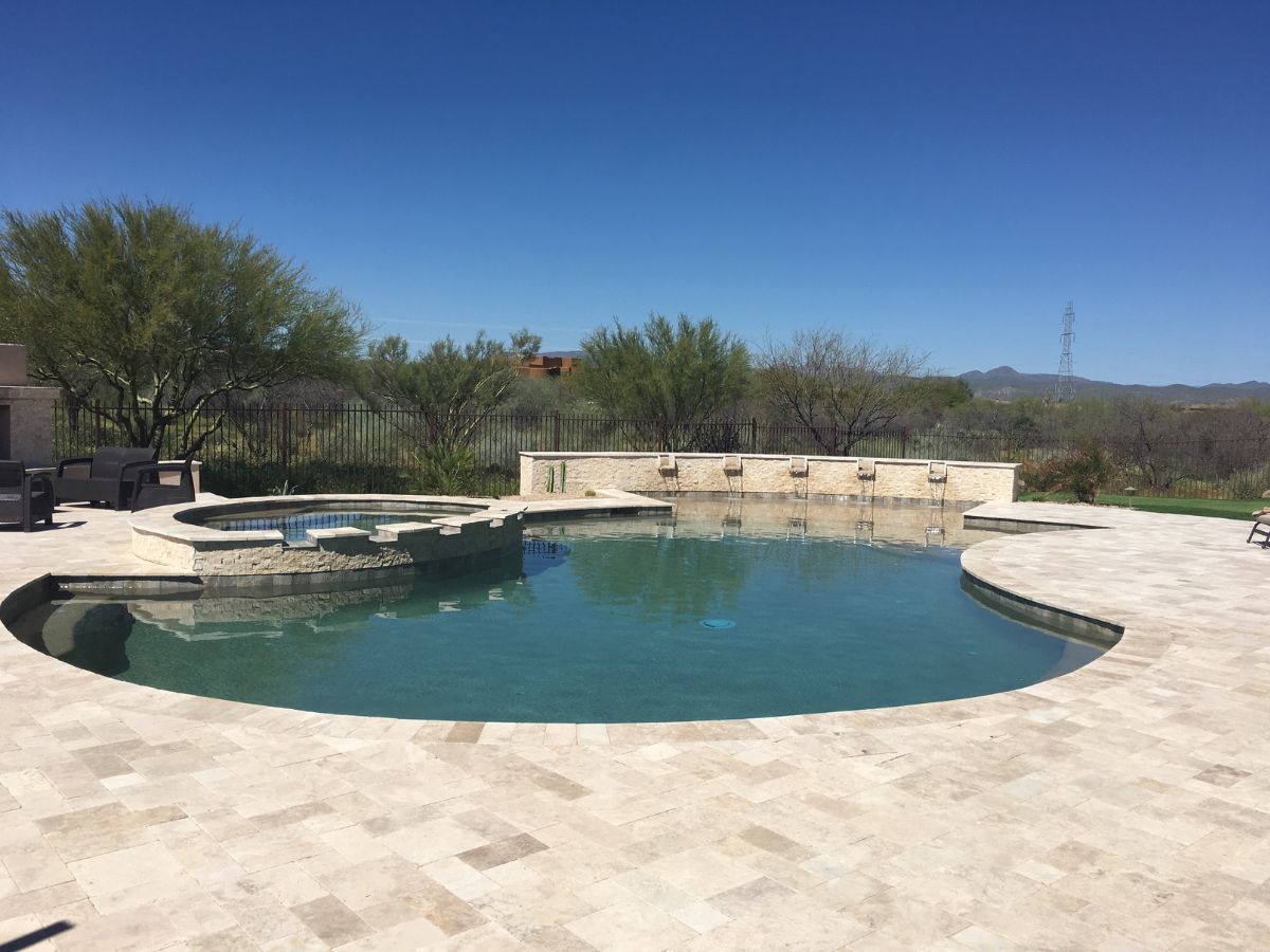 Modern backyard swimming pool with raised spa and travertine deck, desert landscaping and mountain view under clear blue sky