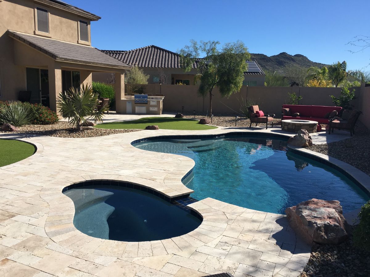 Luxury backyard pool and spa with stone patio, outdoor kitchen, seating, desert landscaping and mountain view