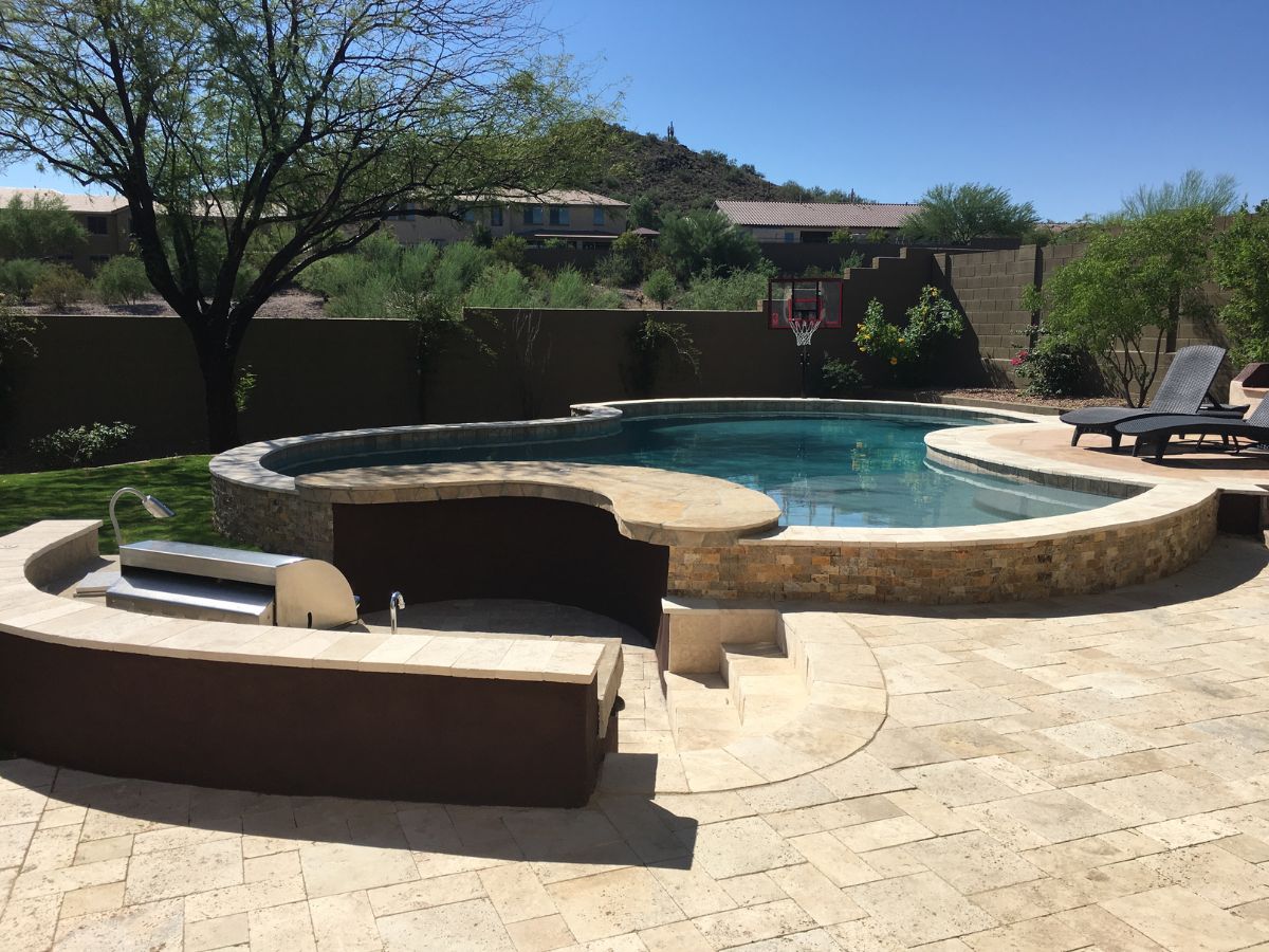 Modern backyard swimming pool design with stone patio, built-in grill, lounge chairs and desert landscaping