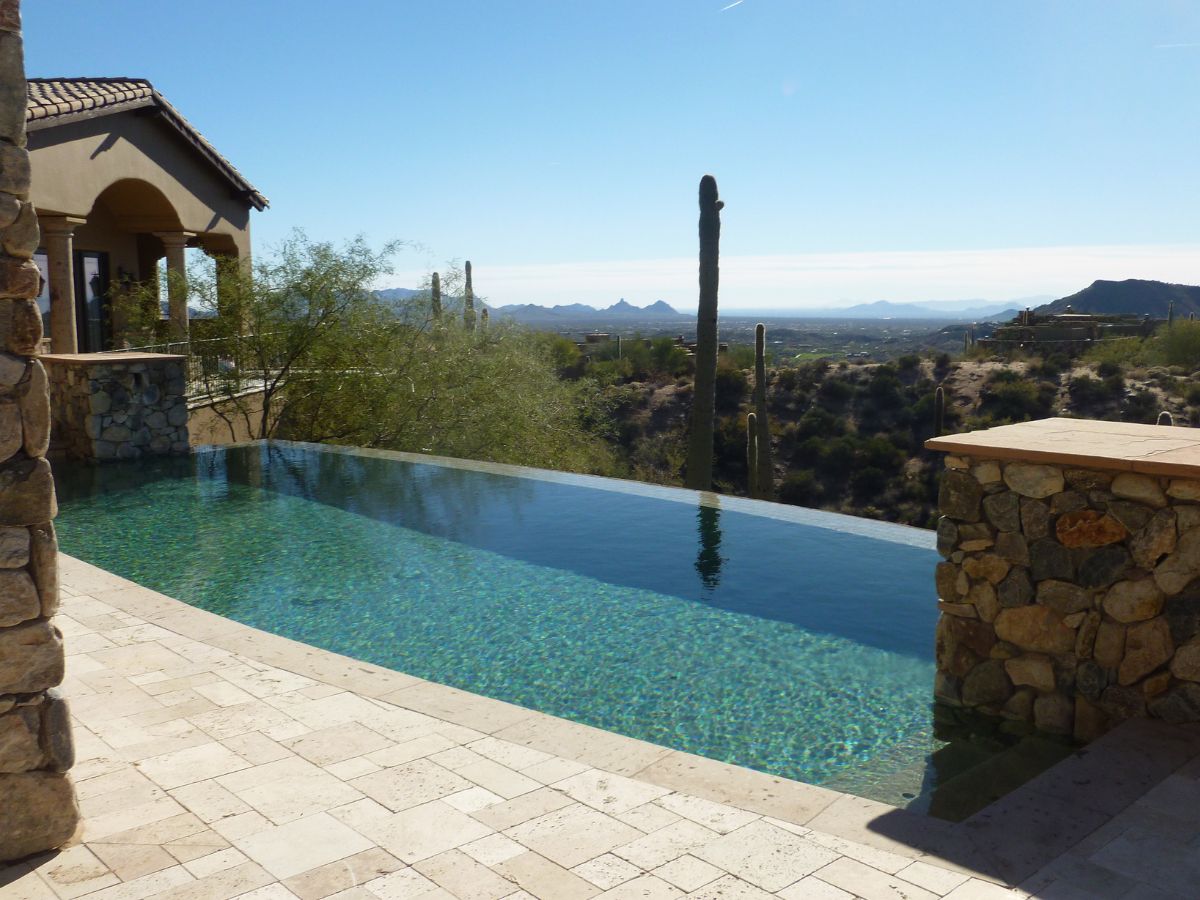 Infinity pool and stone patio at luxury desert villa overlooking saguaro cacti and distant mountains under blue sky