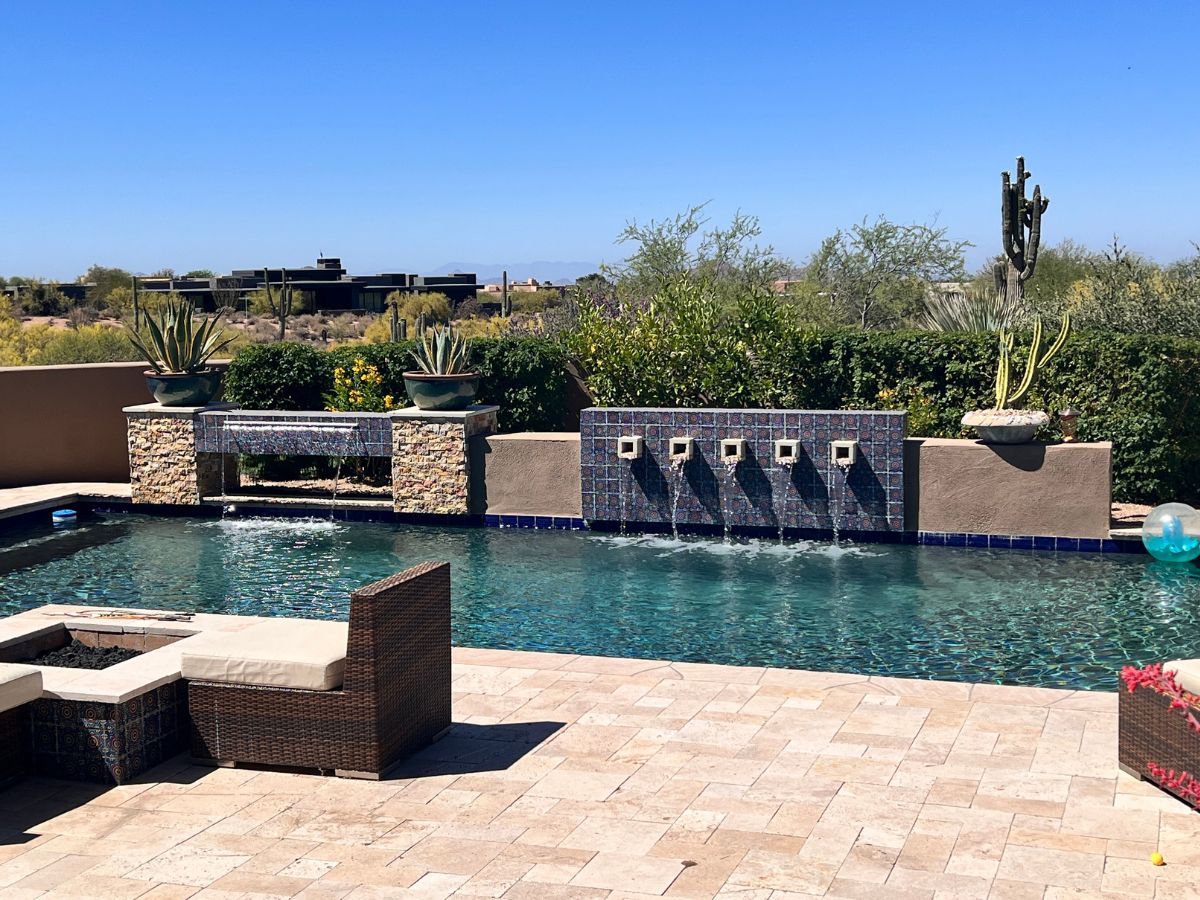 Luxury backyard pool with tiled waterfall features, desert landscaping, cactus and wicker patio seating