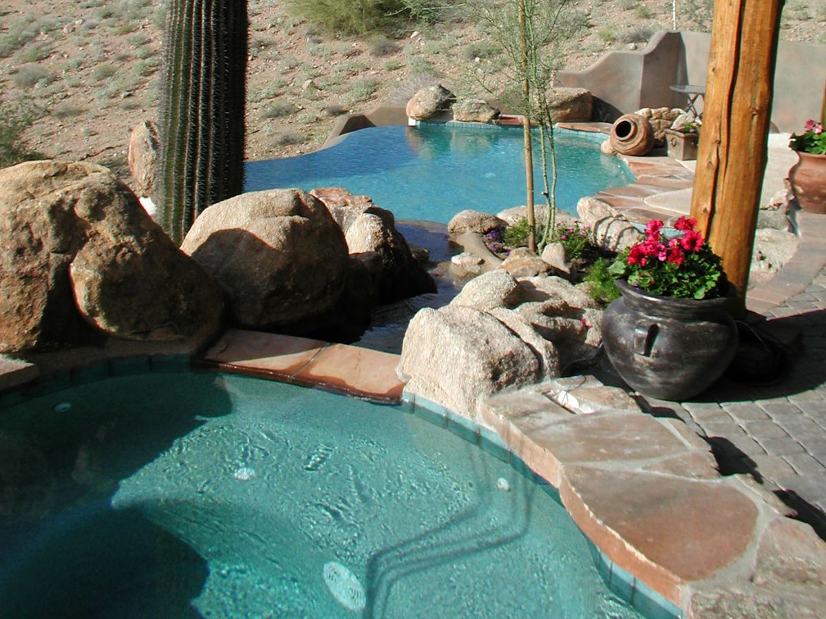 Desert backyard pool and spa with natural rock waterfall, cactus, terracotta pots and pink flowers