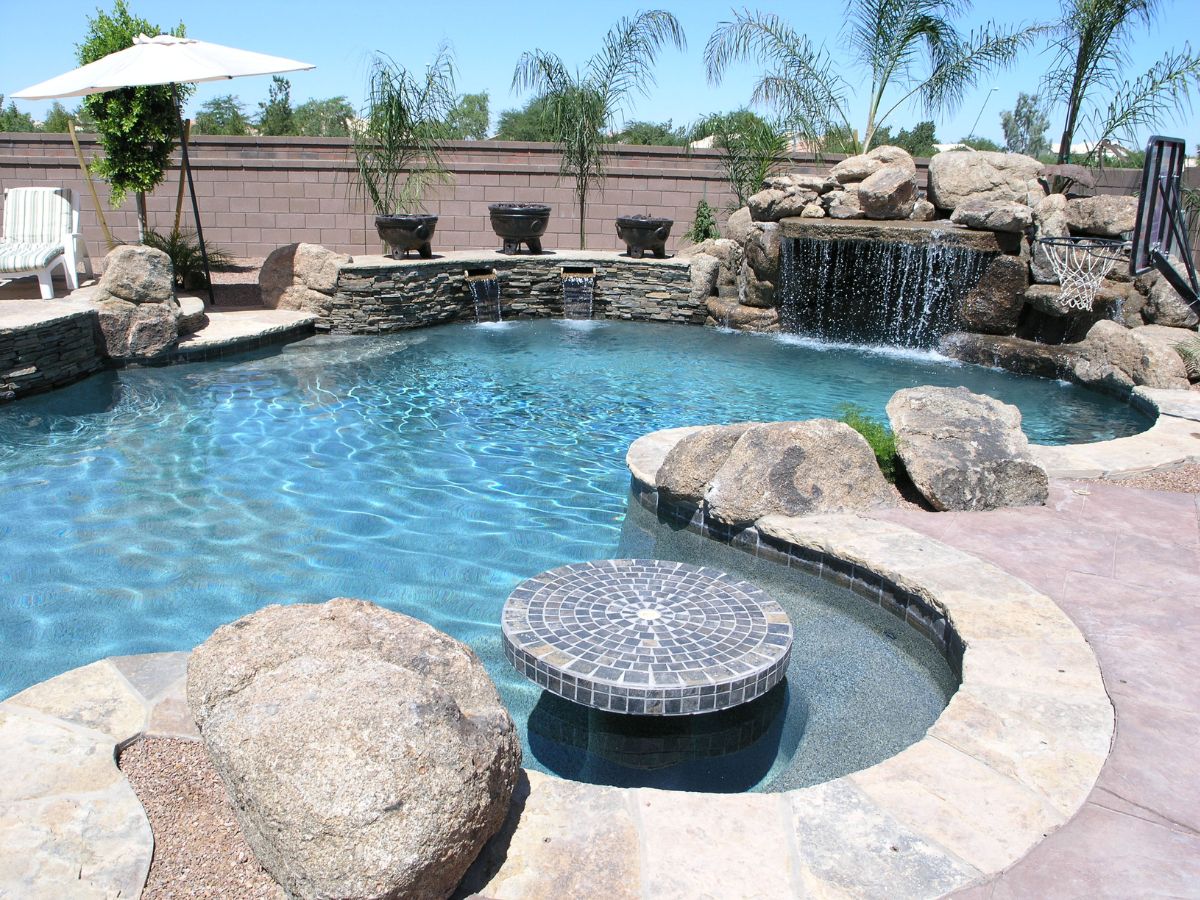 Backyard luxury pool with stone waterfall, in-pool round tile table, rock accents and palm trees