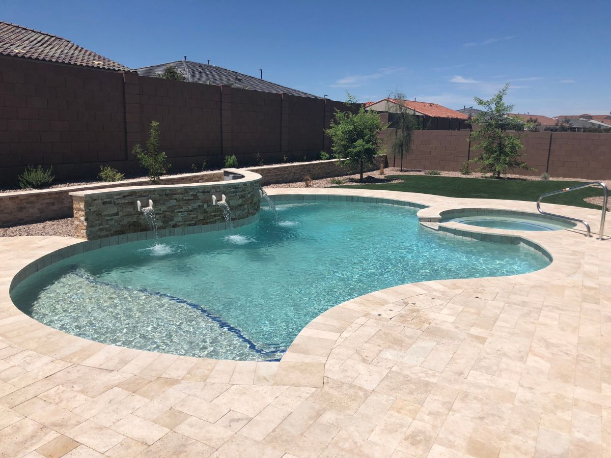 Backyard swimming pool with stone waterfall feature, attached spa, travertine paver deck, and clear blue water