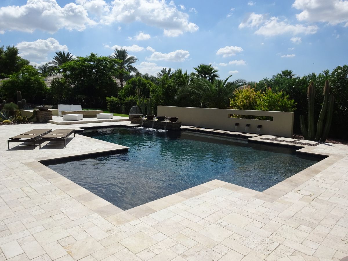 Modern luxury backyard swimming pool with travertine deck, chaise lounges, water features and palm trees