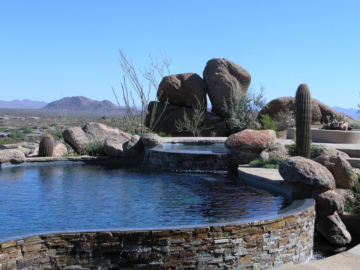 Luxury desert infinity pool with stone waterfall, boulder landscaping, cactus and mountain views