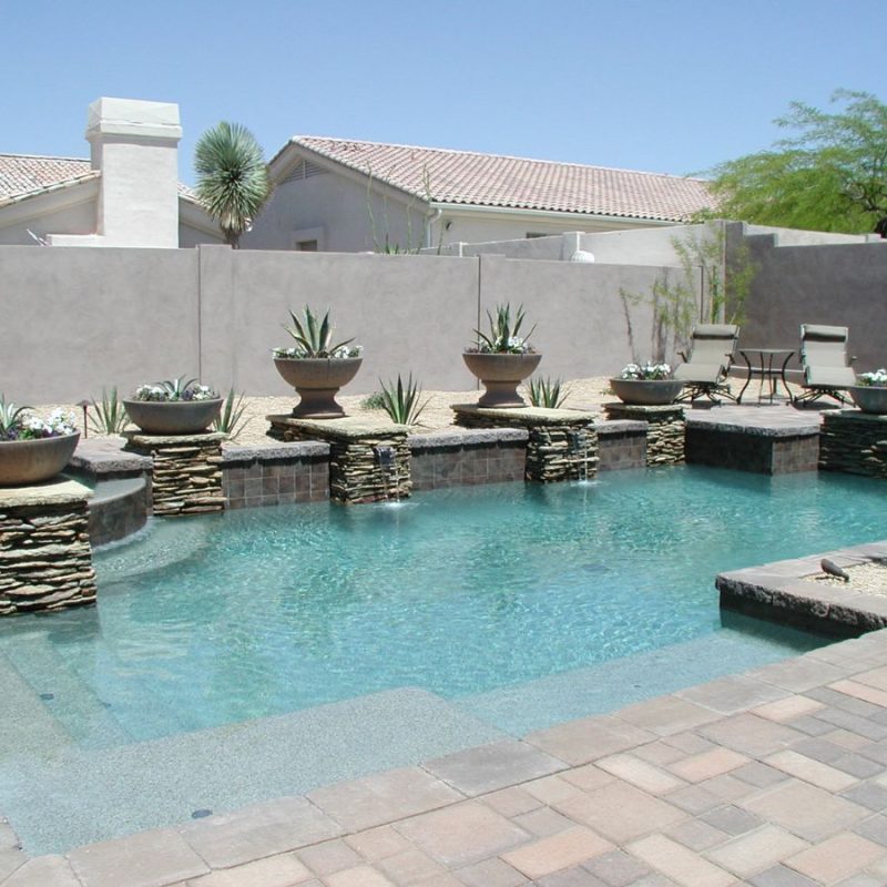 Custom backyard swimming pool with stacked-stone waterfalls, planters, paver deck and lounge chairs in desert landscaping