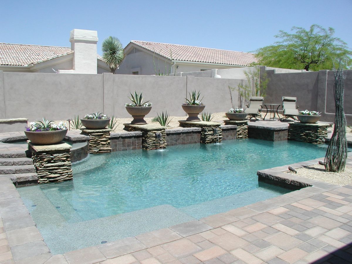 Custom backyard swimming pool with stacked-stone waterfalls, planters, paver deck and lounge chairs in desert landscaping