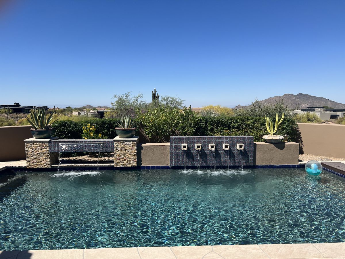 Luxury backyard pool with tiled waterfall spouts, potted succulents and desert mountain view under blue sky