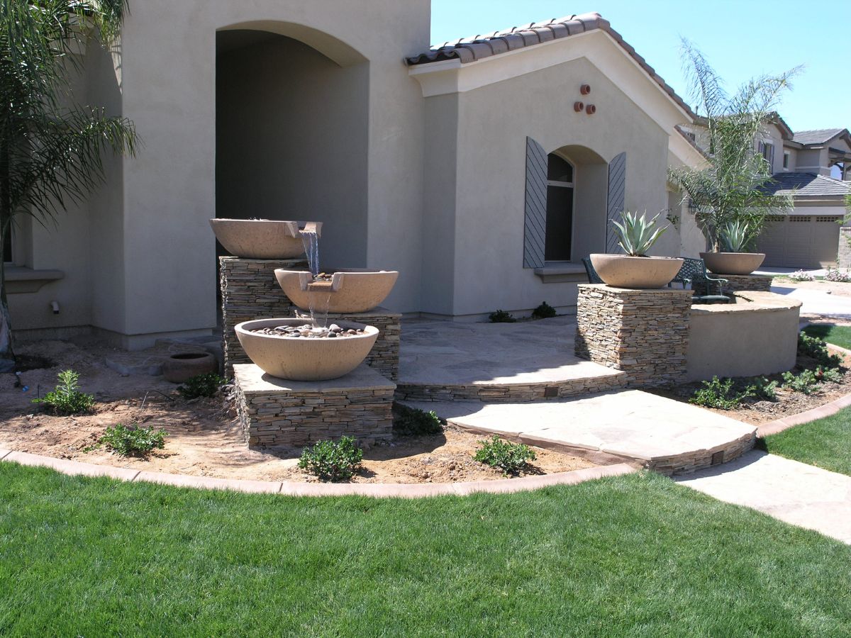 Front yard water feature with stacked stone planters and tiered bowl fountain at a modern stucco home